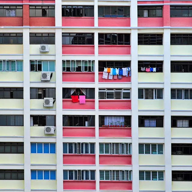 The face of an HDB block in Singapore: rows of windows, laundry poles and an outdoor aircon unit on many of the ledges