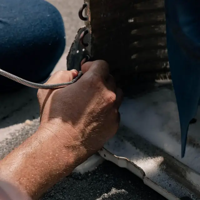 A technician's hand on the copper coil of an outdoor aircon unit during a leak check