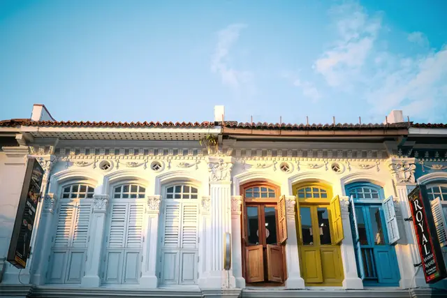 Row of restored shophouse facades with arched timber windows and painted doors in yellow, blue and natural wood