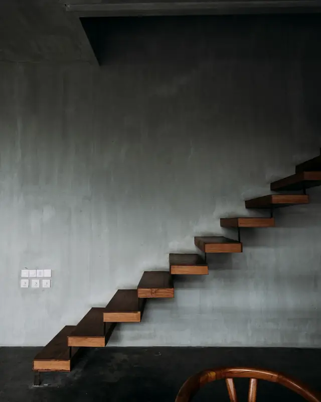 Floating timber staircase cantilevered from a grey fair-faced plaster wall