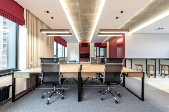 Open-plan office with long timber desks, slatted timber walls and a lit concrete ceiling spine