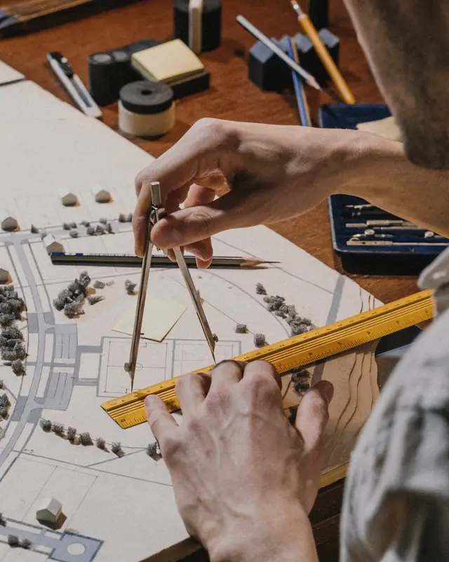 Architect measuring a white site model with a ruler and compass on a drafting table