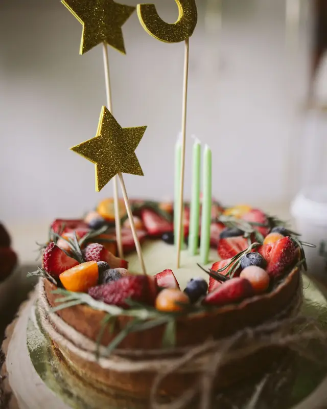 A naked celebration cake topped with fresh berries, candles and gold star toppers