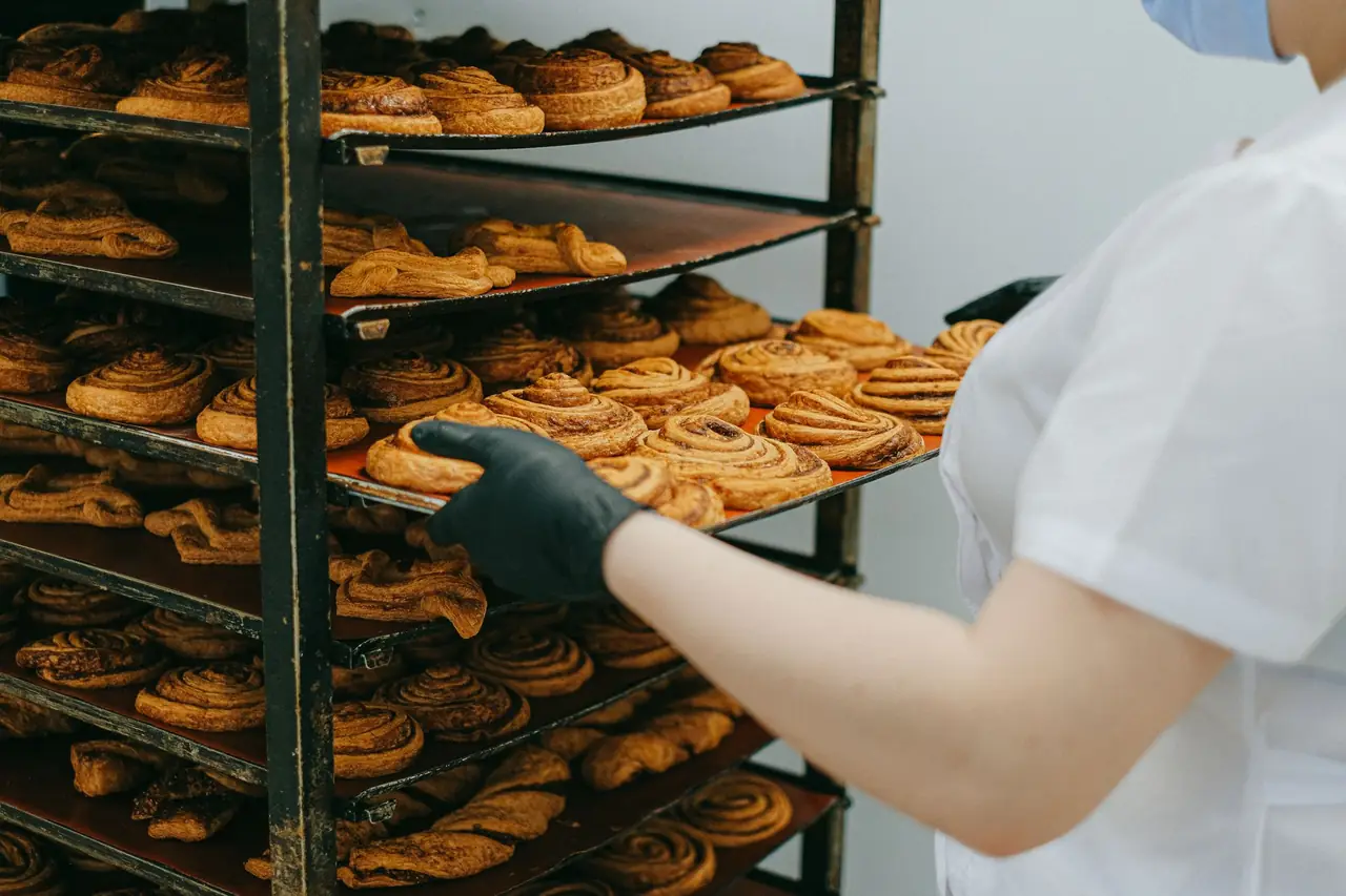 A baker sliding a tray of freshly baked cinnamon rolls onto a tall cooling rack