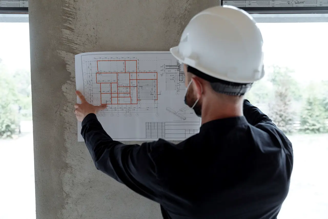 Engineer in a white hard hat checking a floor plan pinned to a column on site