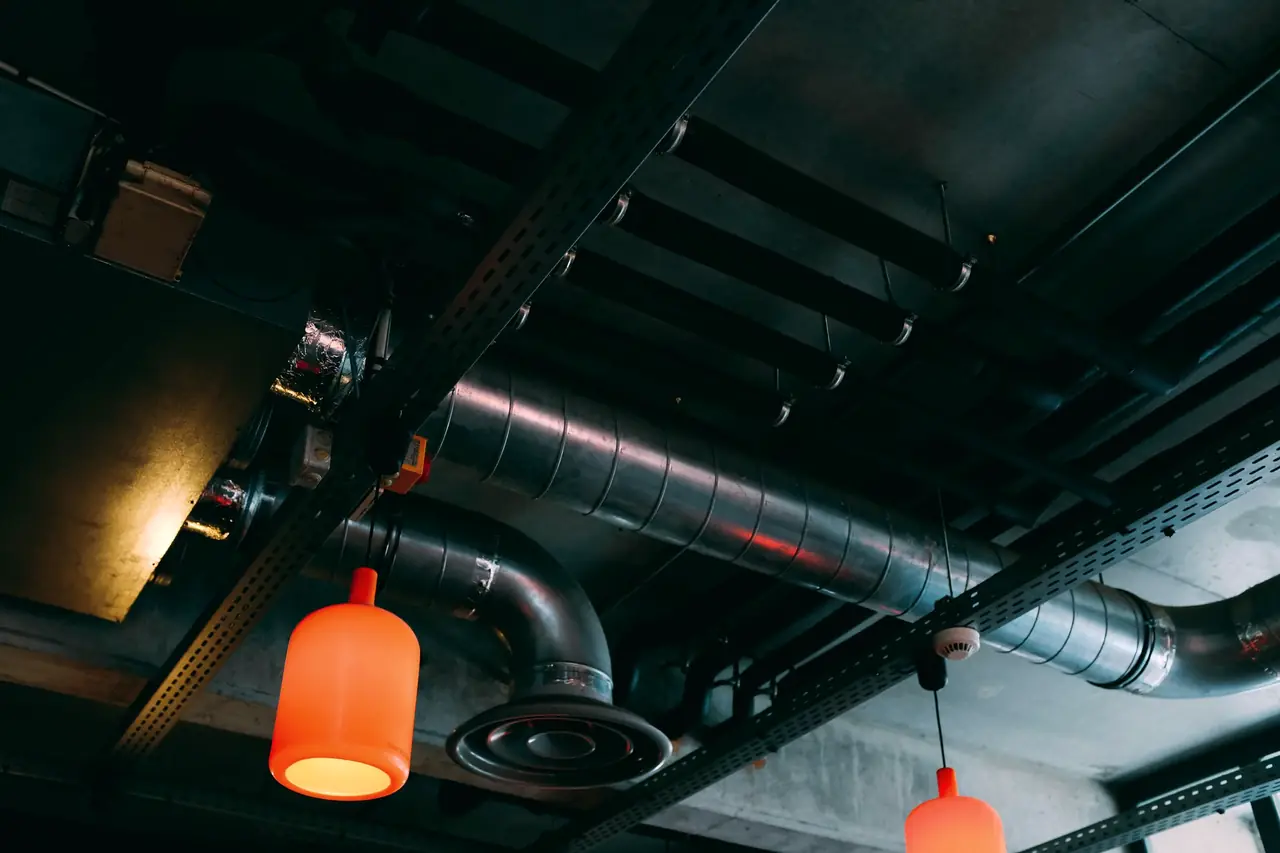 Roastery showroom ceiling with exposed spiral ducting, cable trays and orange pendant lamps