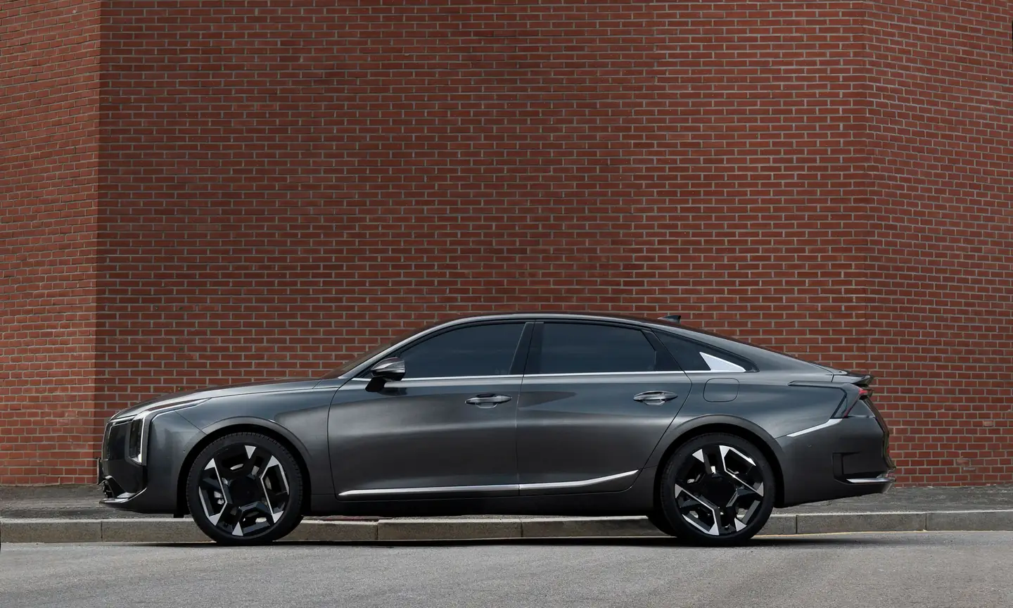 Graphite fastback saloon parked side-on against a red brick wall