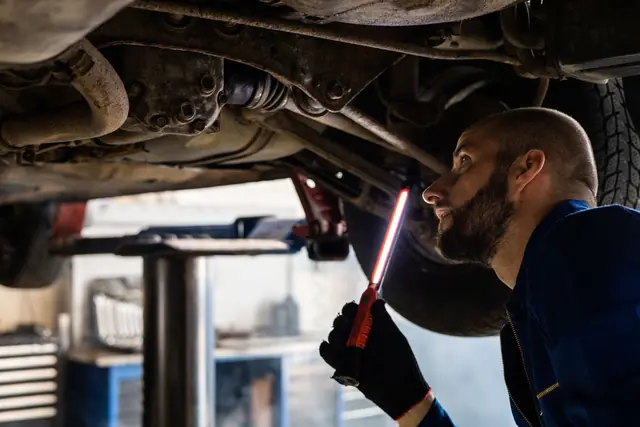 Technician checking the underside of a raised car with an inspection light