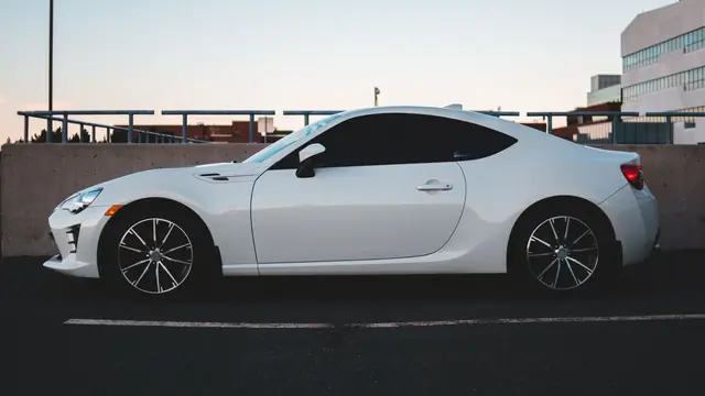 White two-door sports coupé side-on on a rooftop at dusk