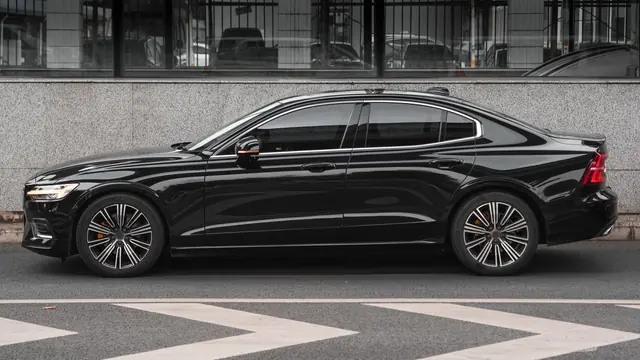 Black sports saloon side-on beside a granite wall, white chevrons painted on the road