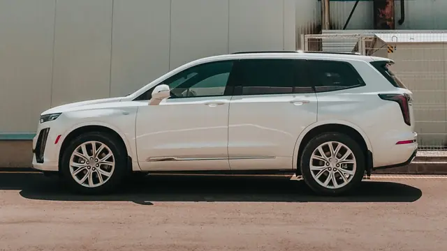 White seven-seat SUV side-on in front of a pale industrial building