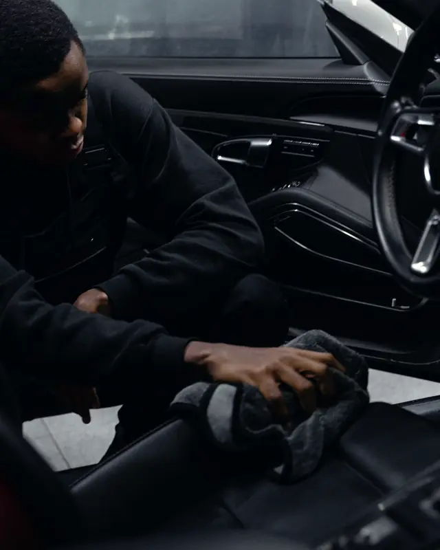 A detailer wiping down a black leather seat inside a dark cabin