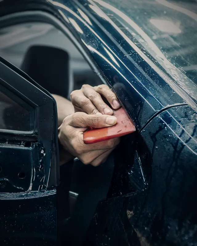 Gloved hands working paint protection film around a door edge with a red squeegee