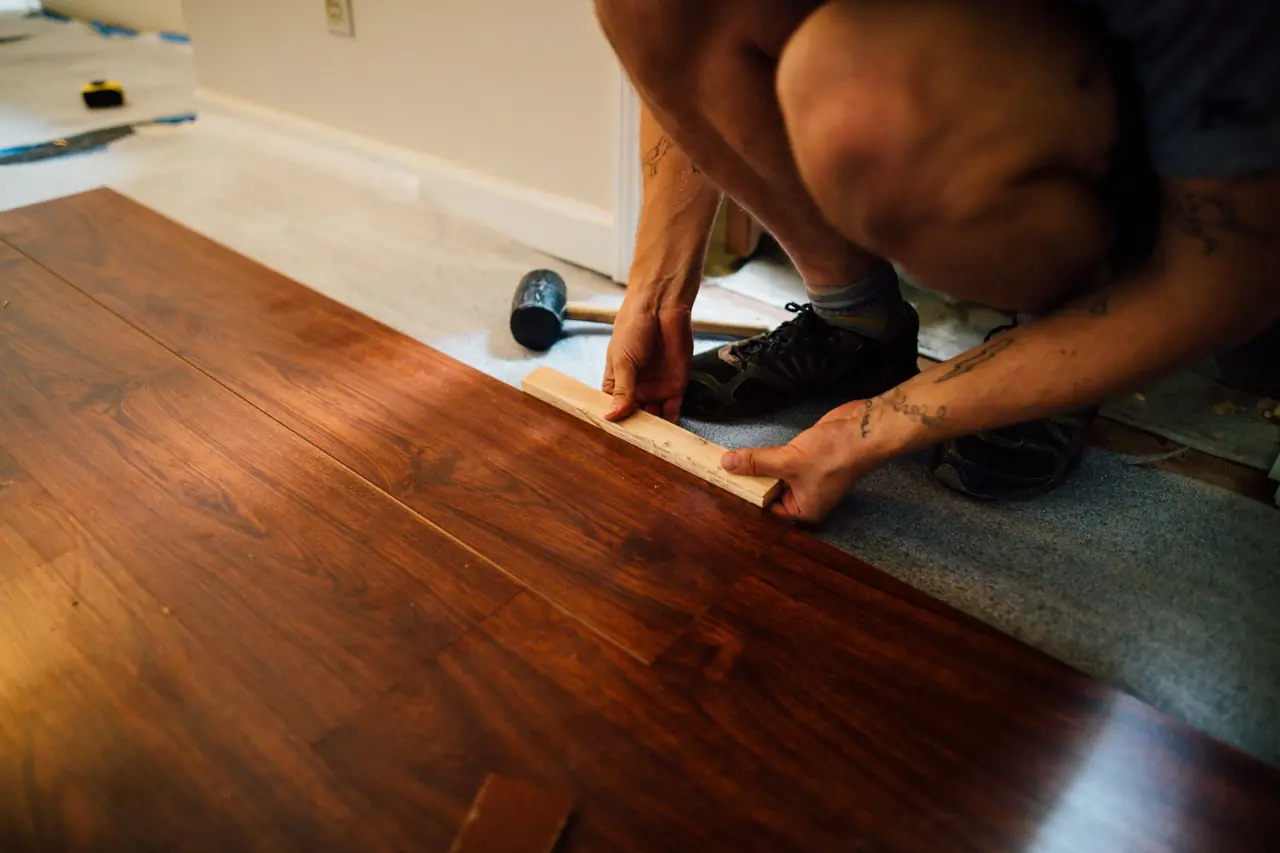 Installer kneeling on an underlay, tapping a wood-look plank into place with a mallet