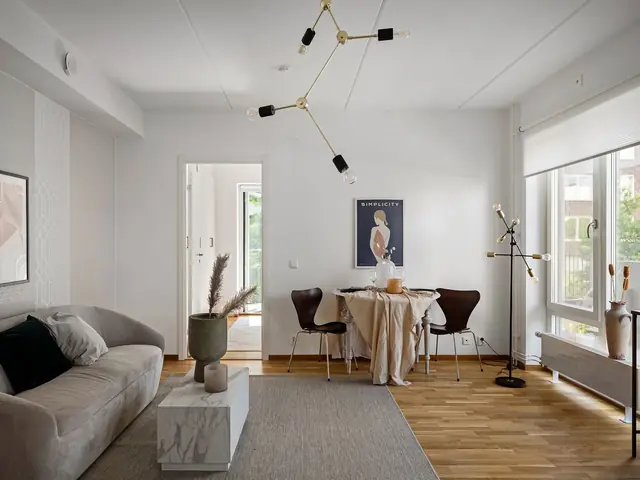 Bright living room with a pale oak-look floor, a grey sofa and a dining table by the window