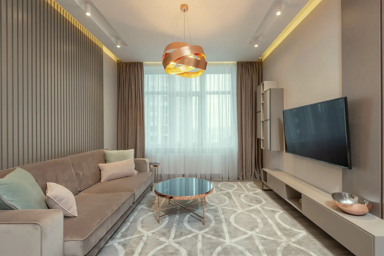 The finished living room: fluted walnut-tone feature wall, linen curtains, a pendant light, a low TV console with a display shelf and a light vinyl floor