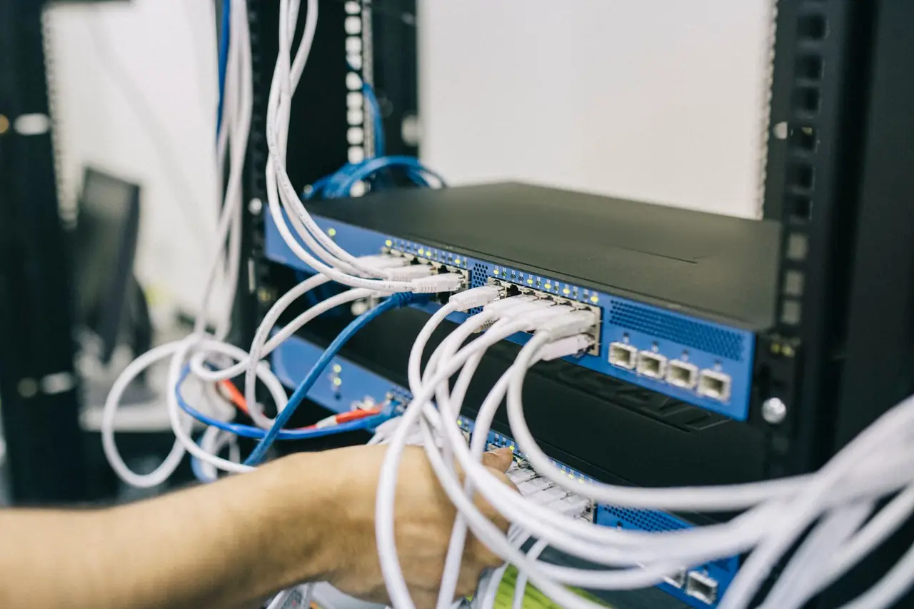 An engineer's hands re-patching white network cables into a new switch in a small office comms cupboard