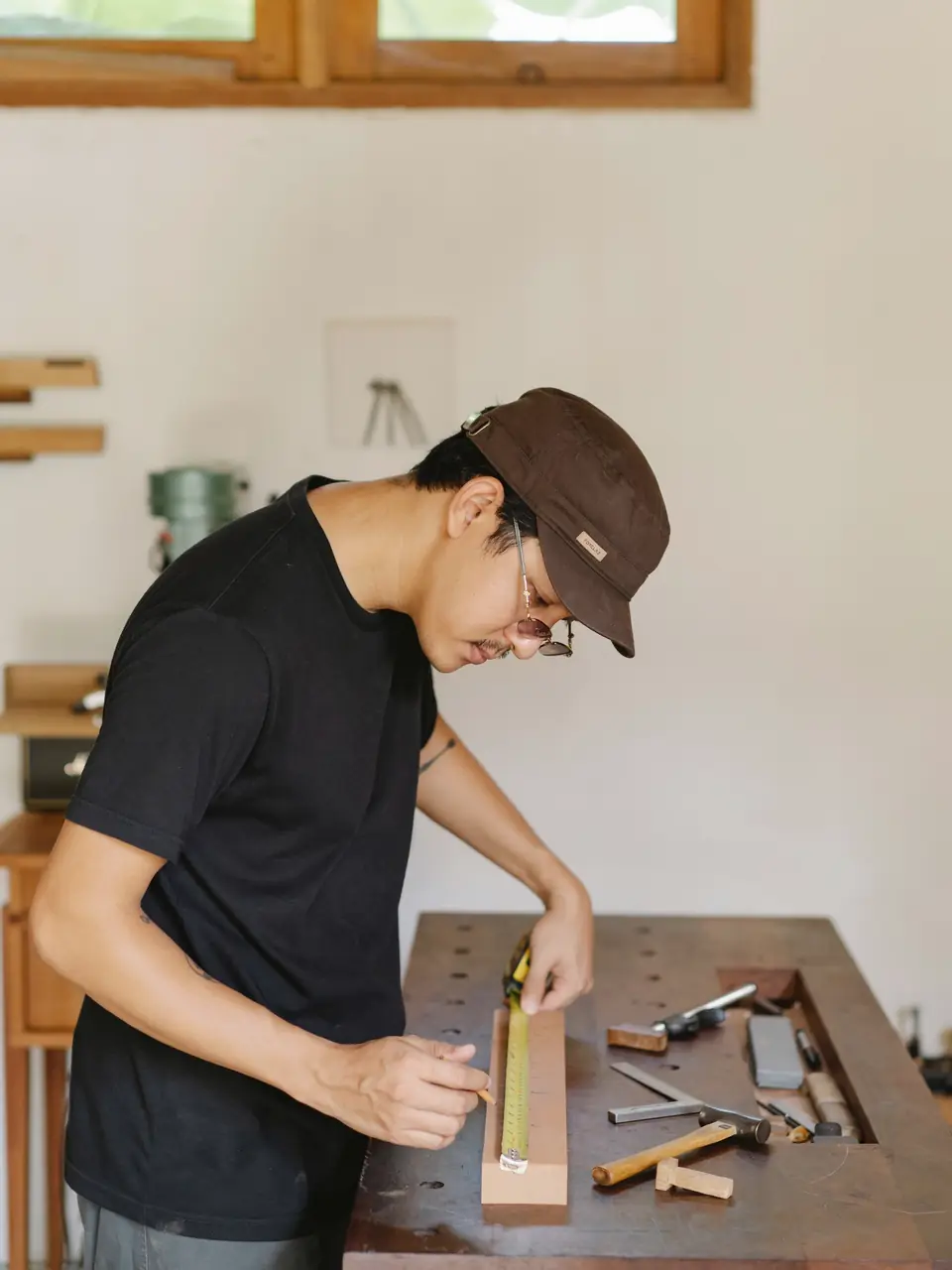 Marcus marking a timber batten with a pencil at a workbench laid out with chisels