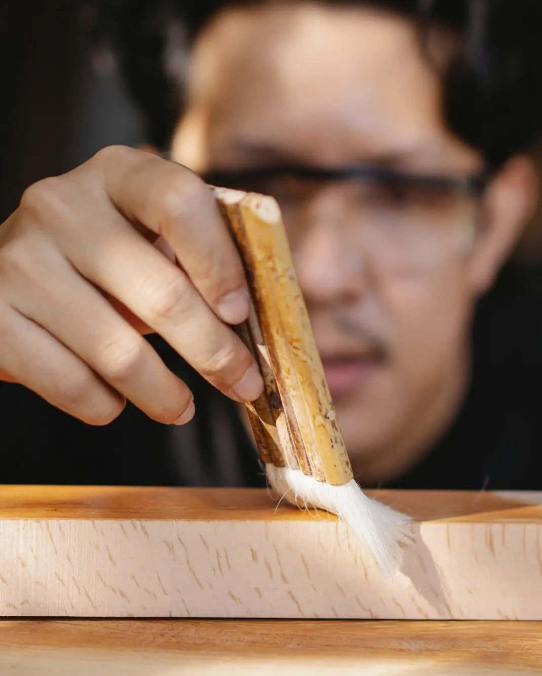 Cabinetmaker brushing a clear finish onto a pale wooden board