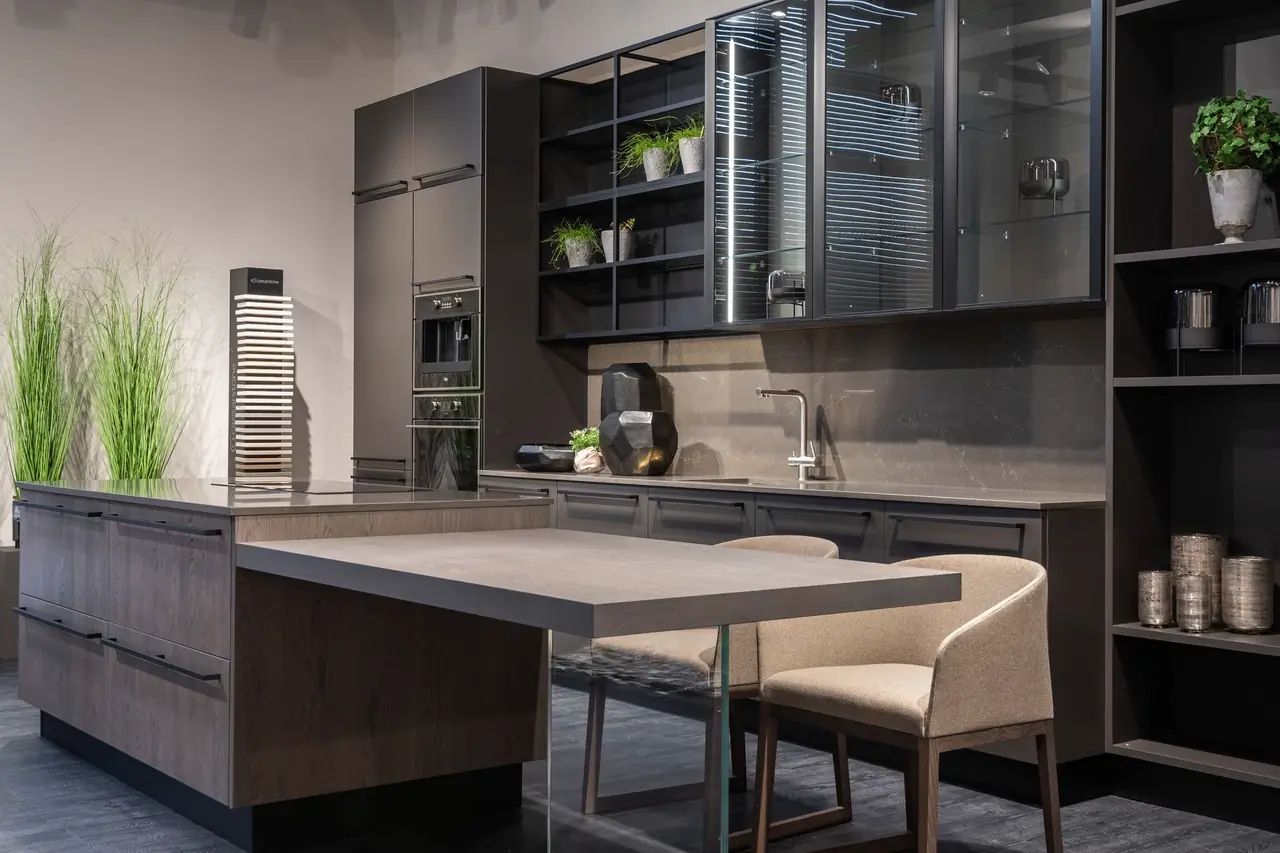 Low-lit kitchen with a walnut-grain laminate island, dark wall cabinets and glass-fronted display units