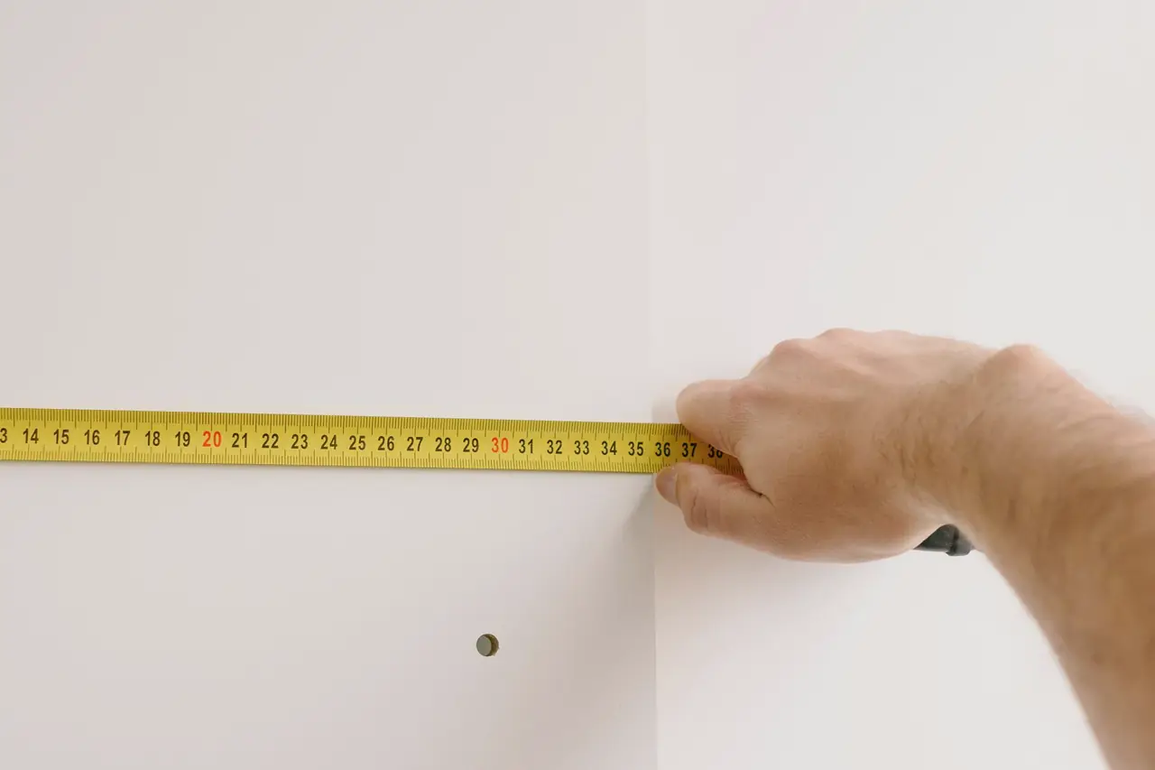 A hand holding a steel tape measure across a white wall