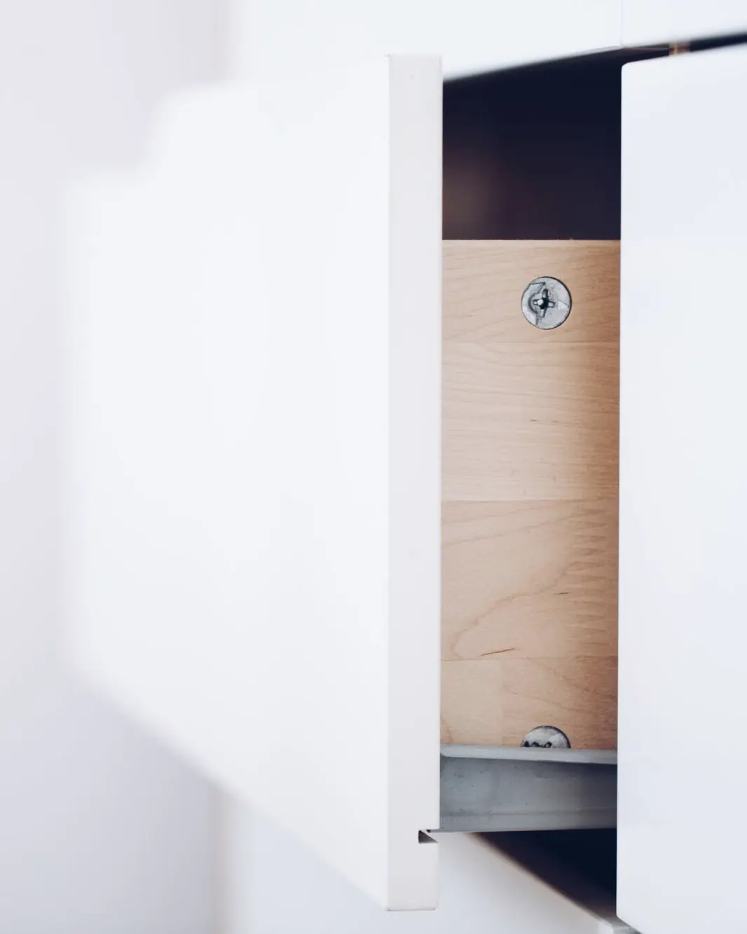 A white drawer pulled half open, showing its plywood side and the metal runner beneath