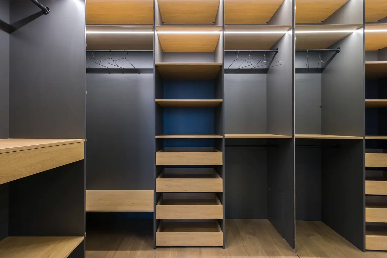 Walk-in wardrobe in dark grey with oak drawers, open hanging bays and a lit top shelf