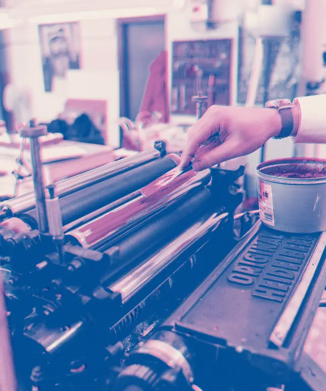 A printer brushing fresh ink onto the rollers of an old press