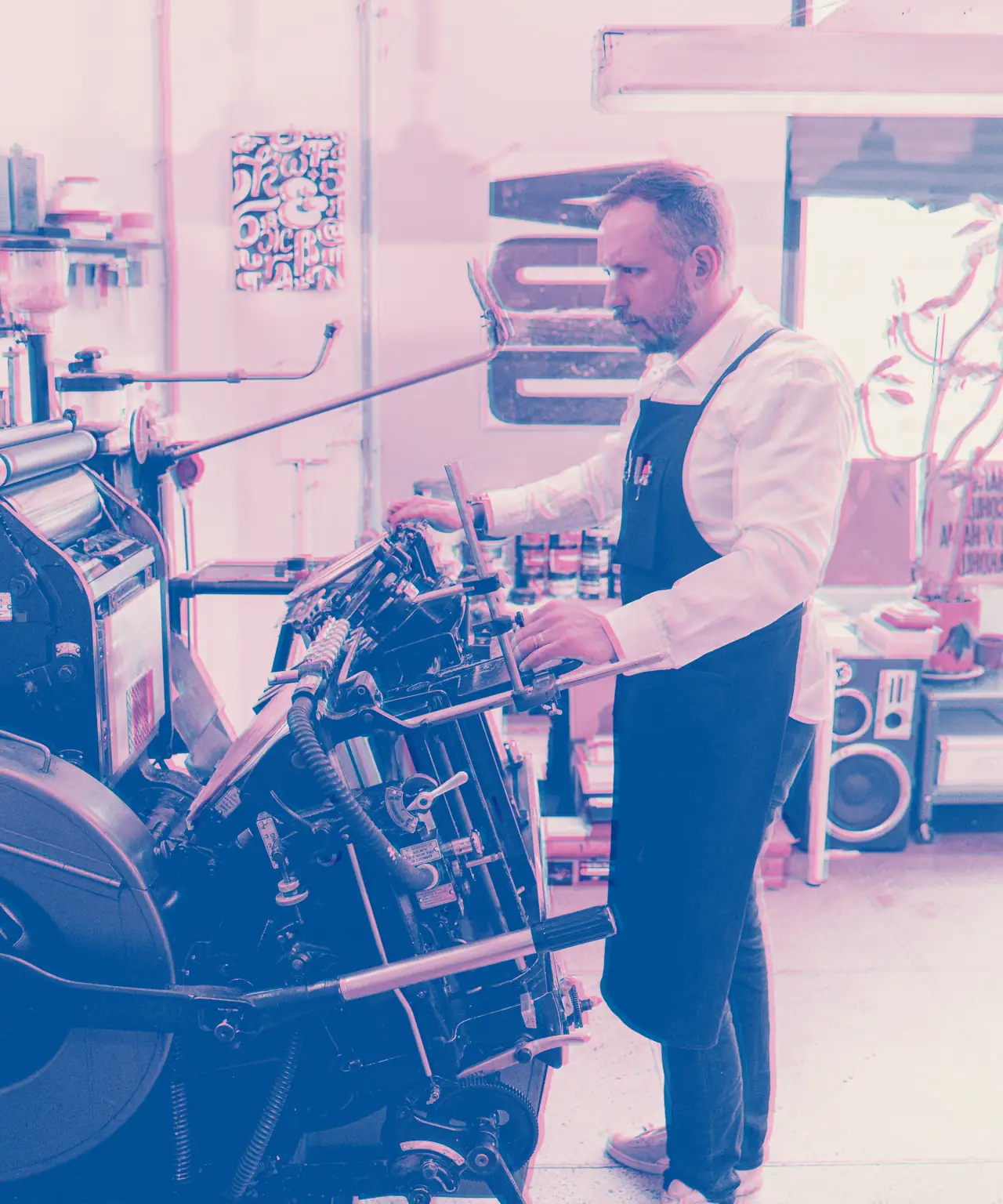 A printer in a work apron setting up a large platen press on the shop floor