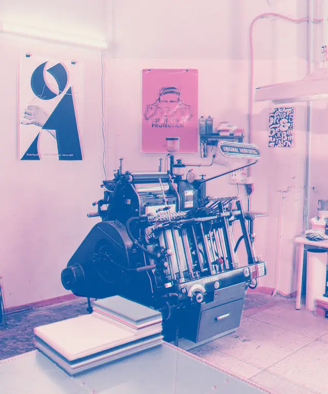 Print studio with a platen press, stacked paper and posters pinned to the wall