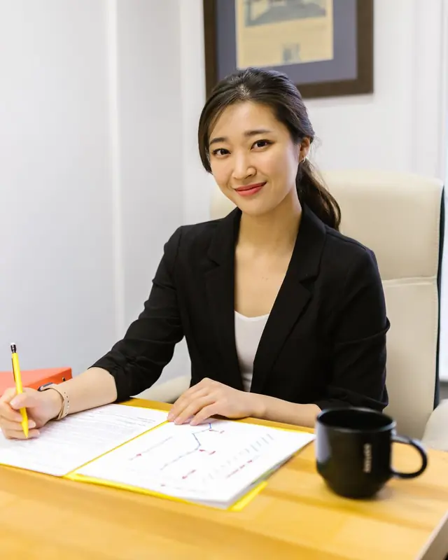 Evelyn Seah smiling at her desk, pen in hand, with an open report and a black mug