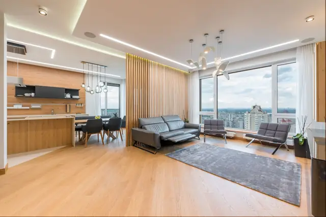 A bright condo living room with oak floors, a grey sofa and floor-to-ceiling windows over the city