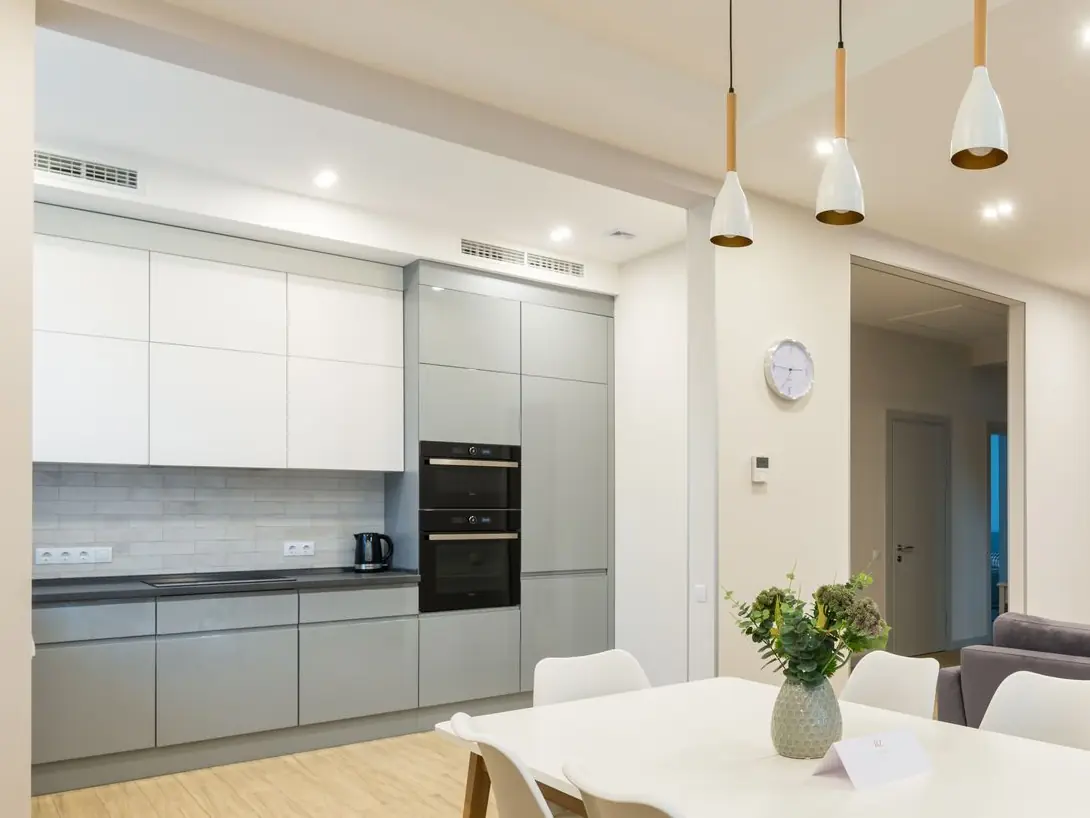 Open kitchen with grey and white cabinets beside a white dining table, where the old kitchen wall used to stand