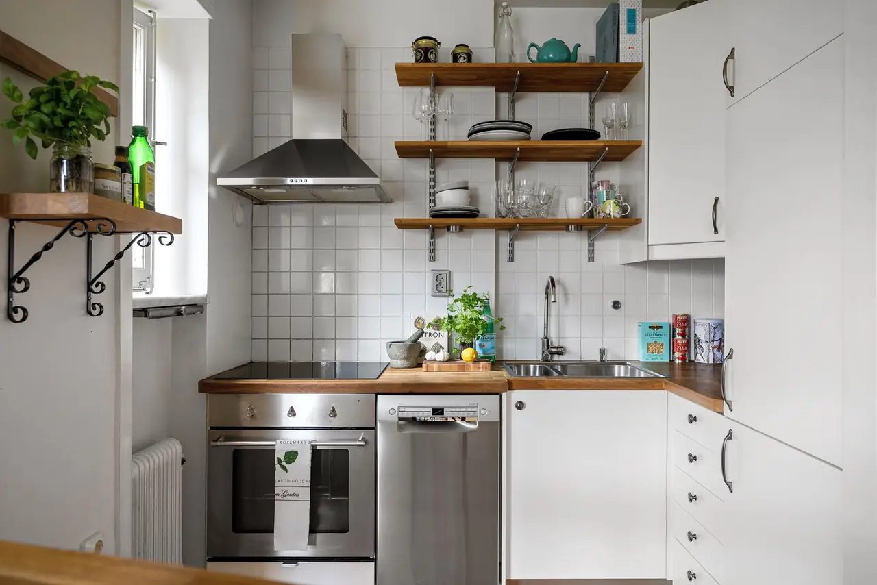 White kitchen with open timber shelves, a steel cooker hood and square white wall tiles