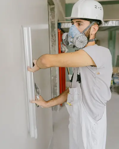 A worker in a mask and white overalls fitting a door frame
