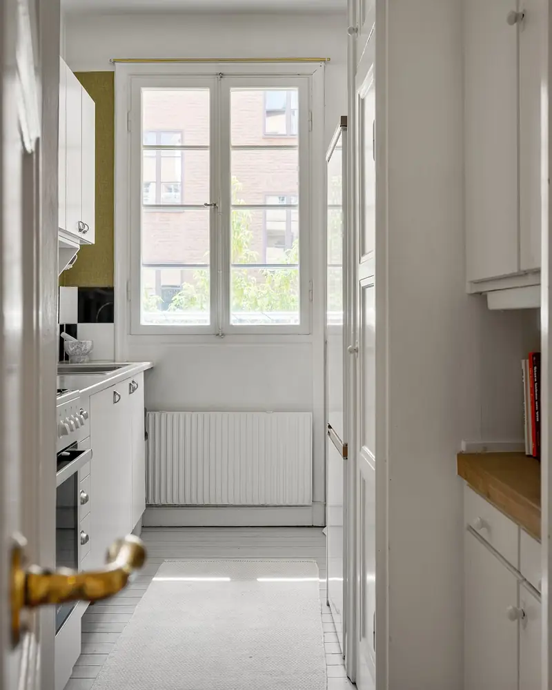 Narrow white galley kitchen leading to a window at the far end