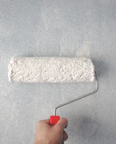 A hand rolling white paint onto a grey wall