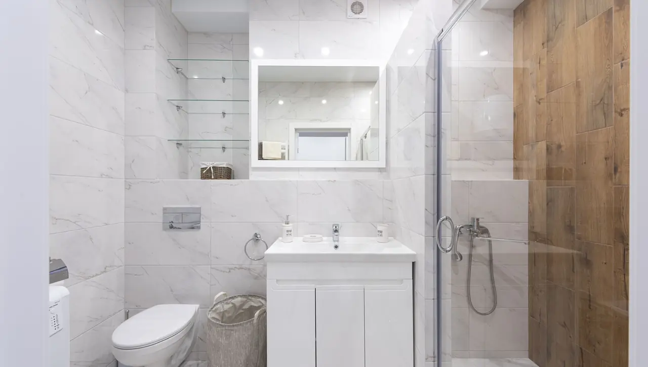 White marble-look bathroom with a glass shower screen, wall-hung toilet and a white vanity