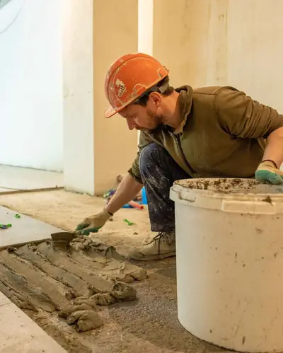 A tiler in a hard hat setting floor tiles into fresh mortar