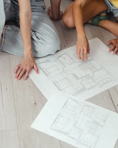 Two people kneeling on a floor over printed floor plans