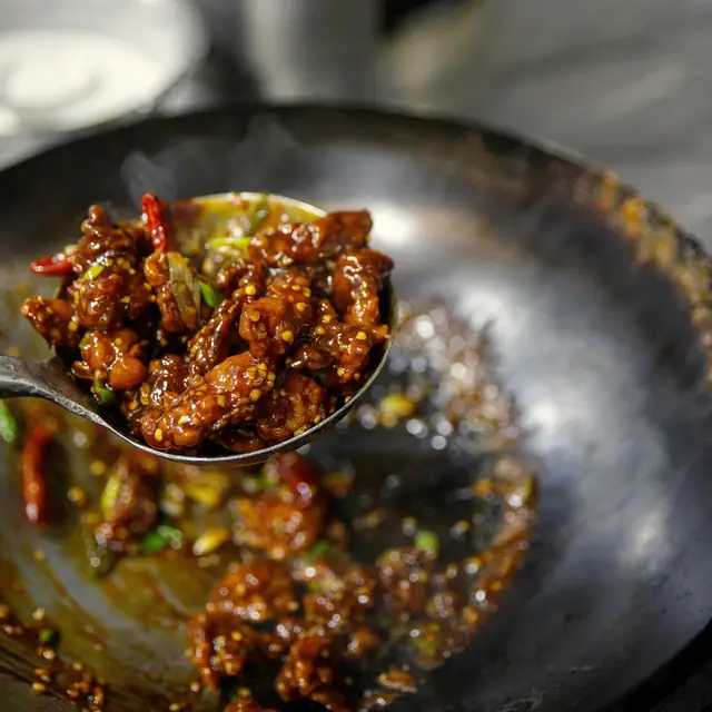 Glossy black pepper beef lifted out of a wok on a ladle
