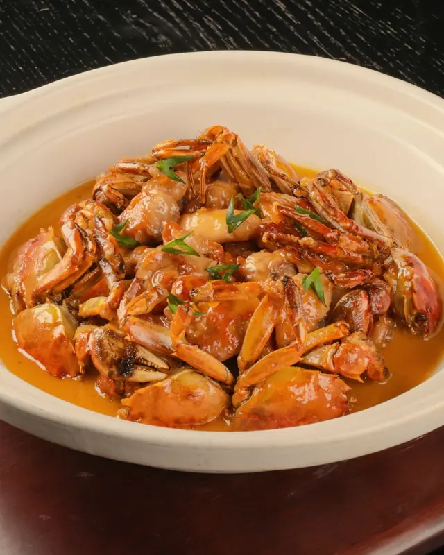 Crab in a thick chilli gravy, served in a white claypot on a dark table