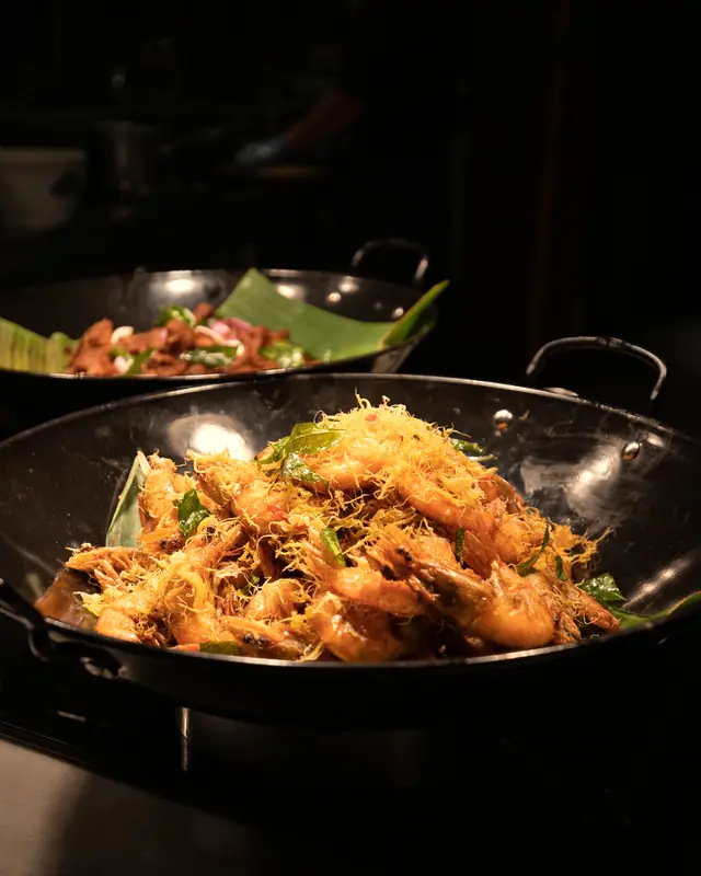 Cereal prawns piled in a black wok under warm light