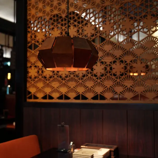 A carved timber lattice screen and a copper lamp glowing over a dark dining room