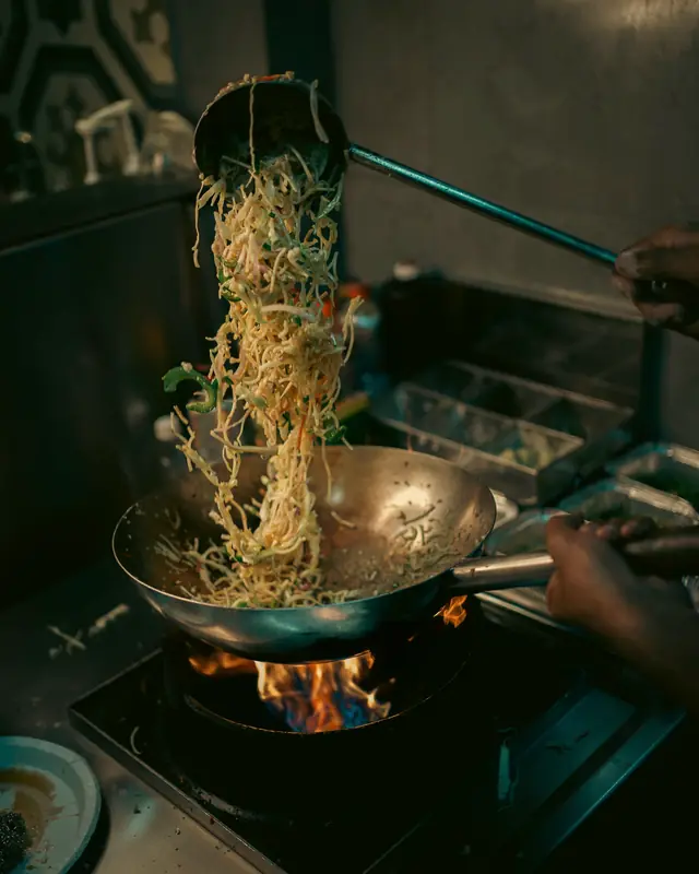 Noodles thrown up out of a wok over a gas flame