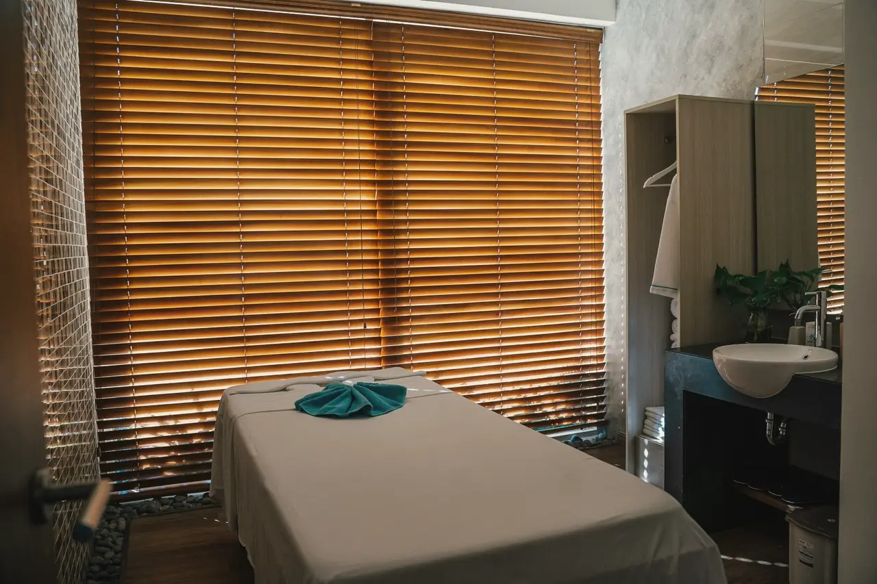 An empty treatment bed by wooden blinds, afternoon light coming through.
