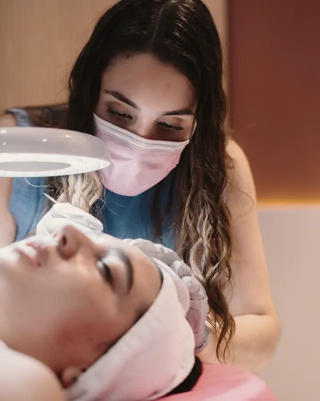A therapist looking through a magnifying lamp at a guest's skin.