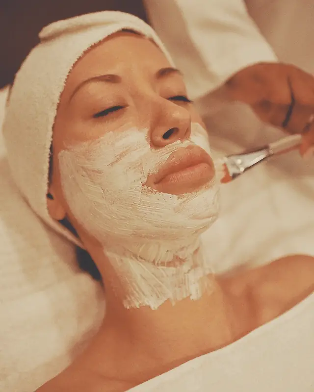 A white mask being brushed onto a guest's face and neck.