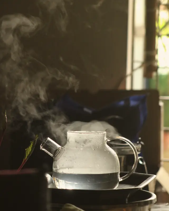 A glass teapot steaming by a window.