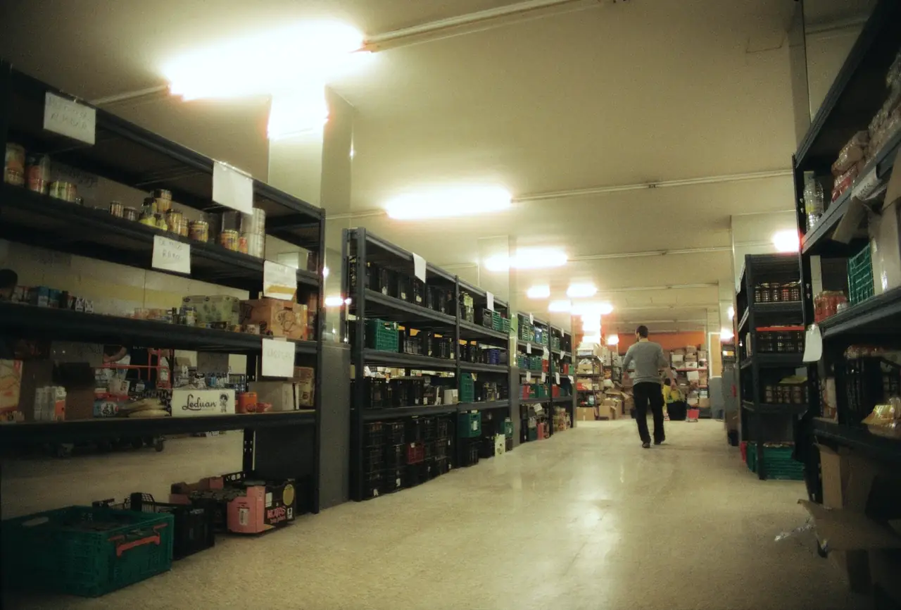 A long warehouse aisle lined with shelving and stock, a worker walking at the far end